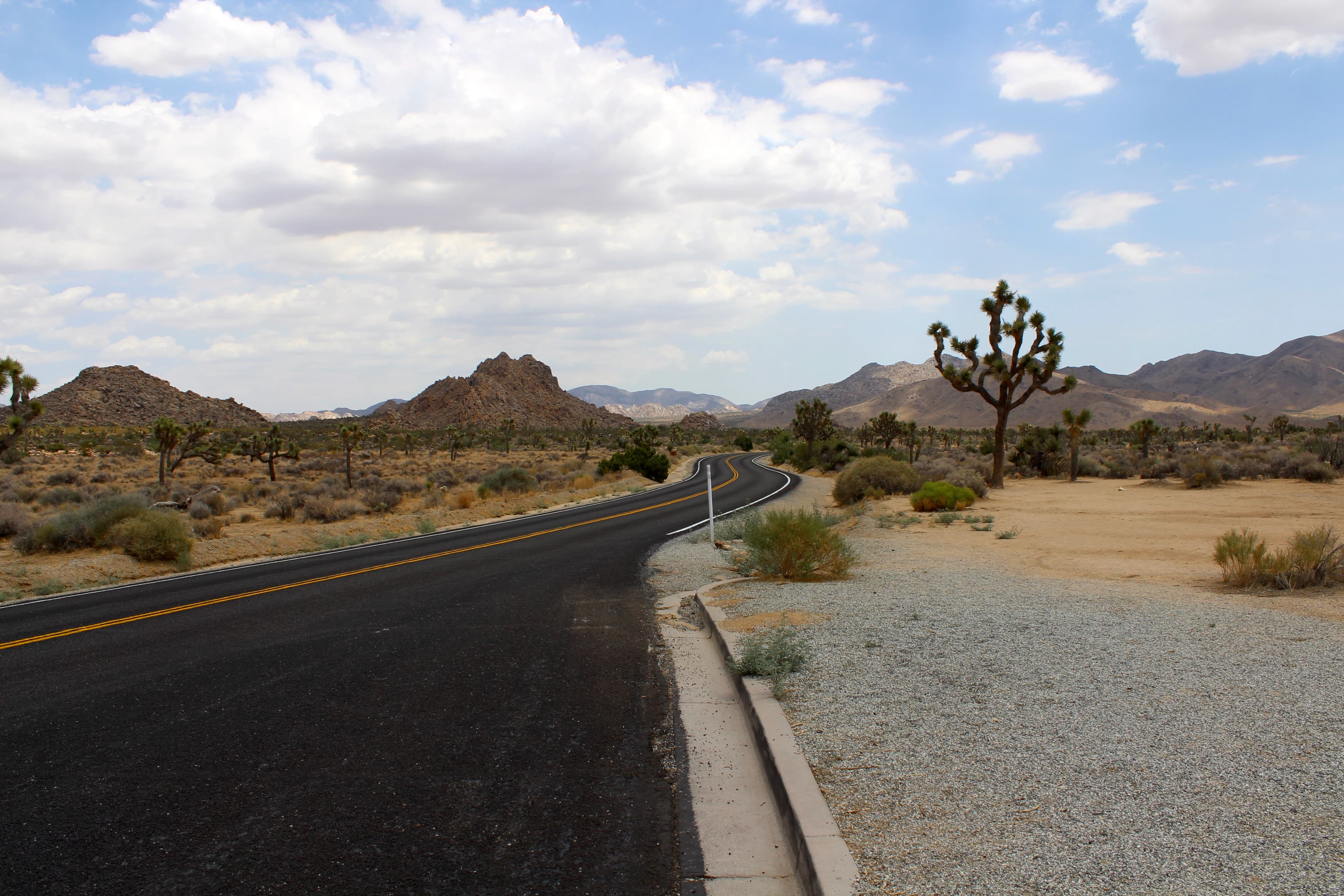 gray concrete road near brown mountain under white clouds during daytime