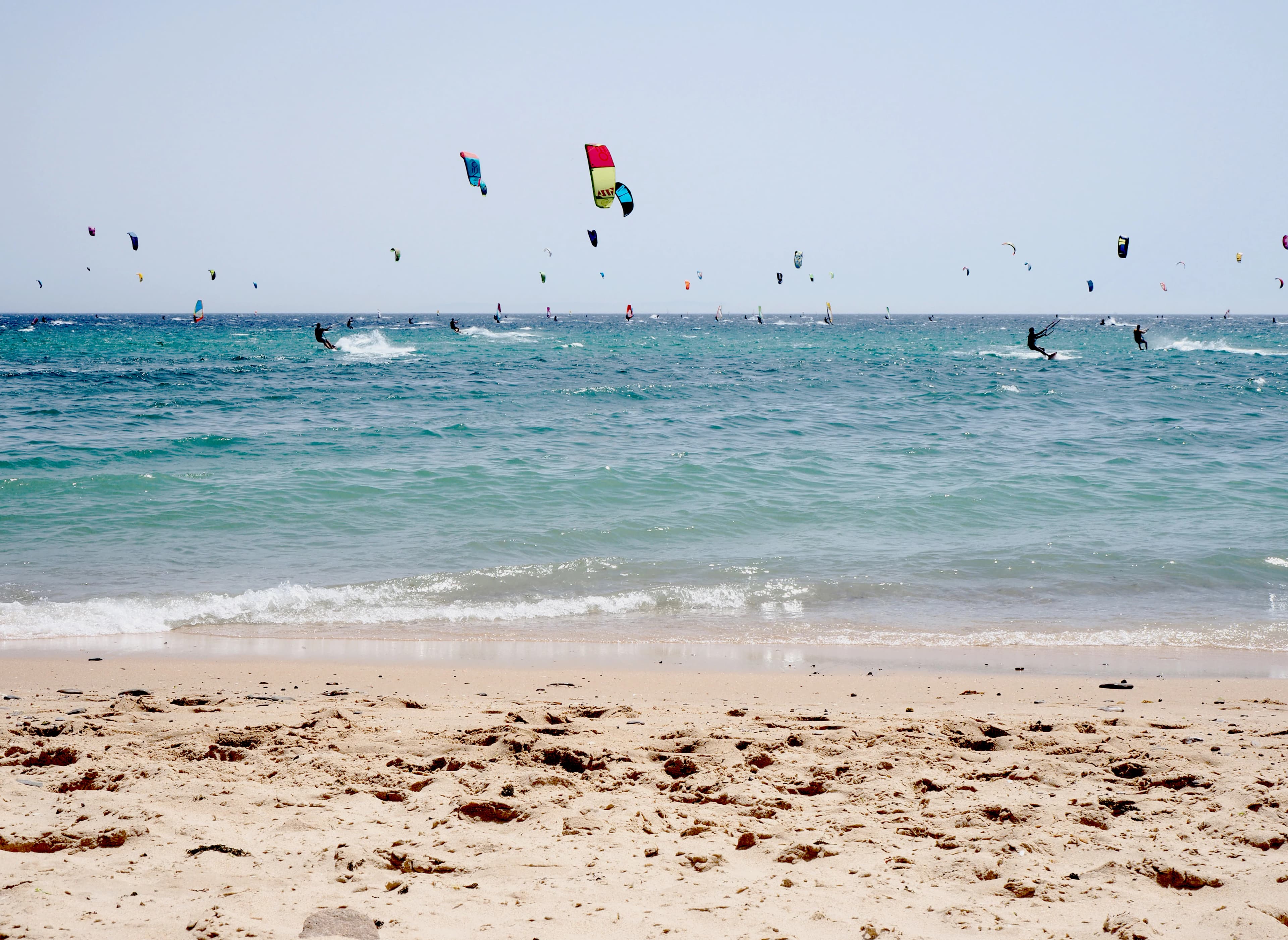 a group of people flying kites on top of a sandy beach