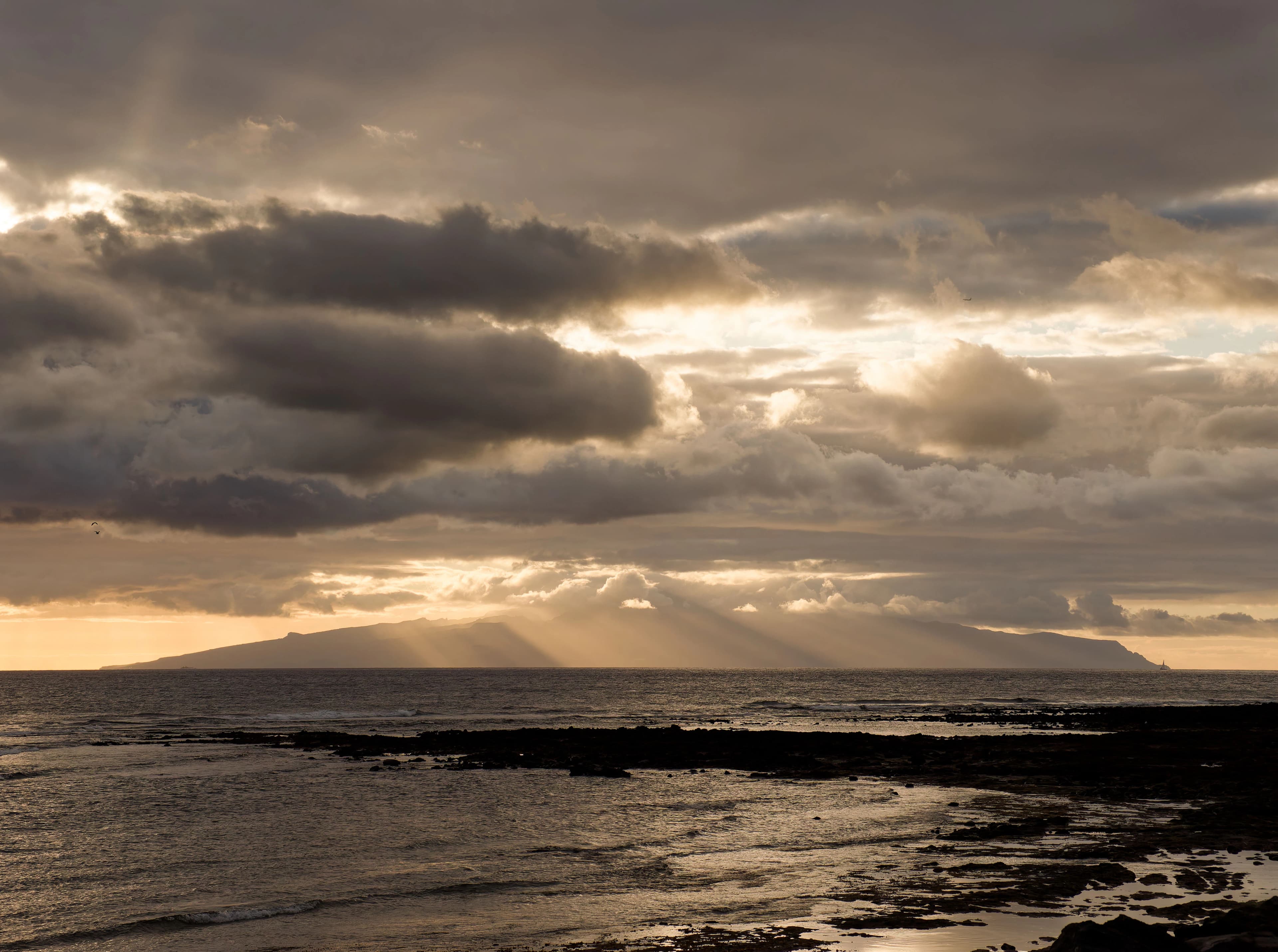 Sunbeams breaking through clouds over ocean and island.