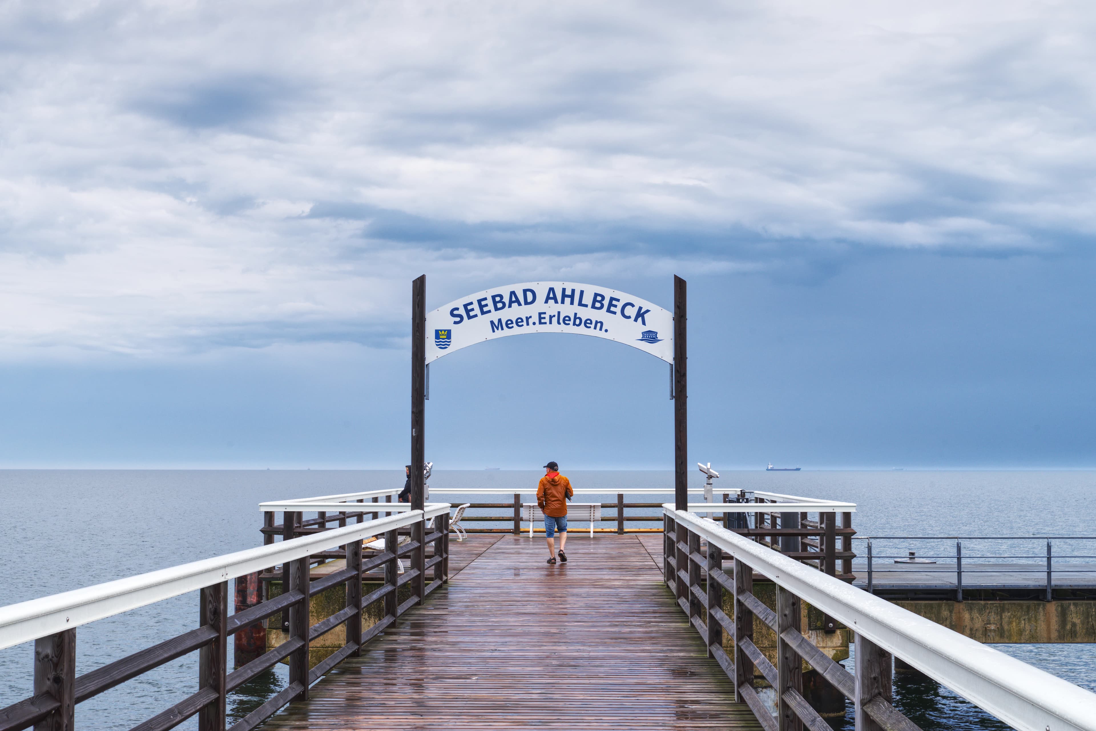 Man walks on pier towards archway over the sea.