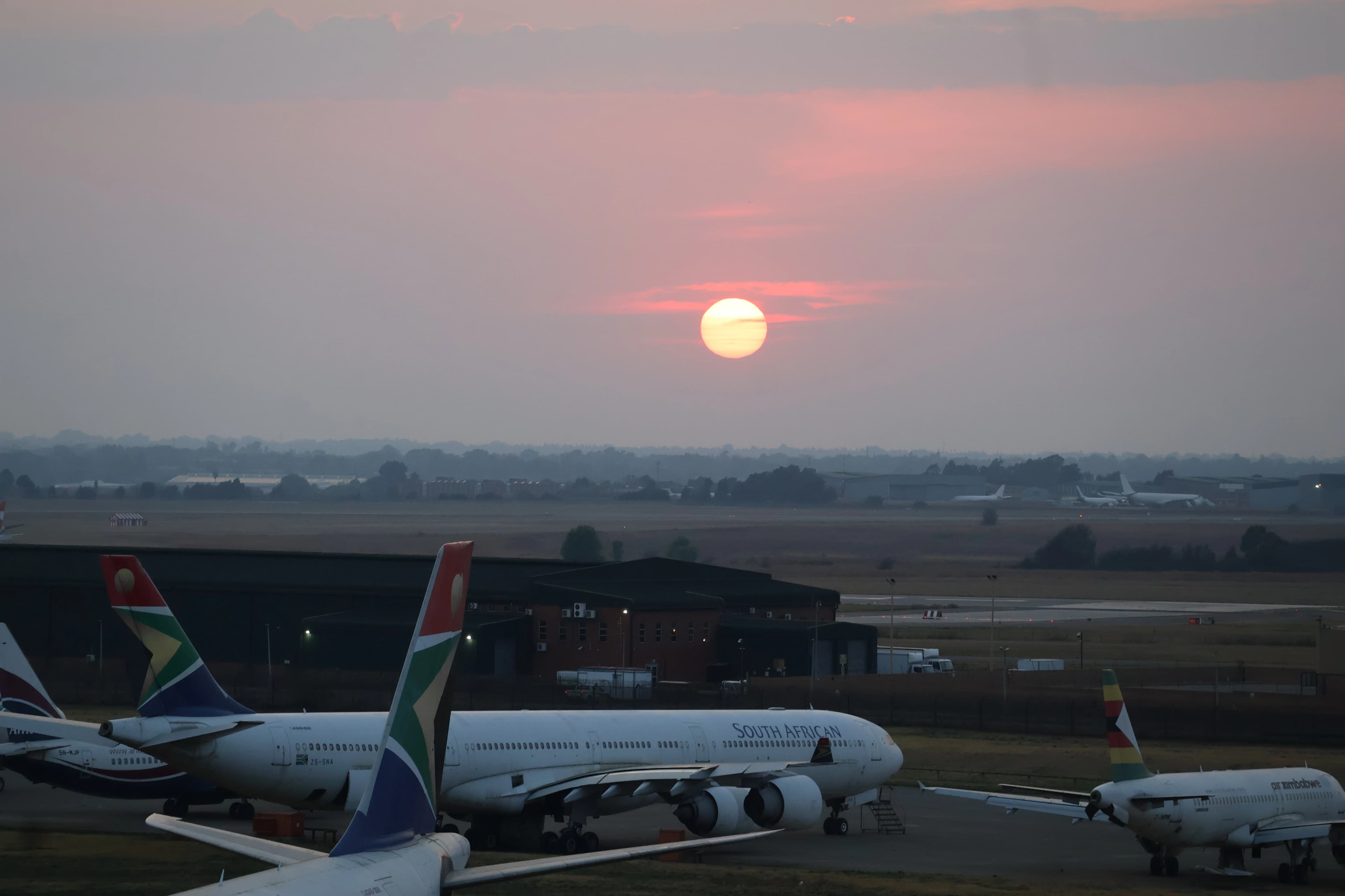 Sunrise over an airport tarmac with parked airplanes.