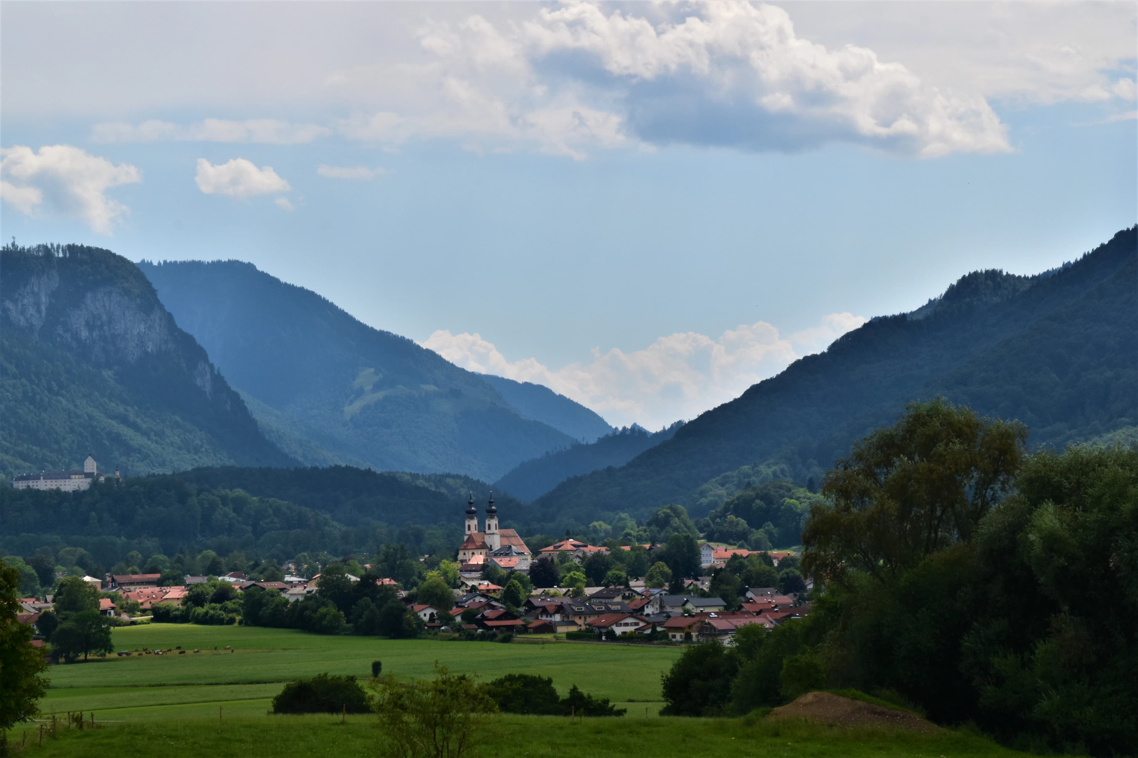 green grass field near green mountains under white clouds during daytime