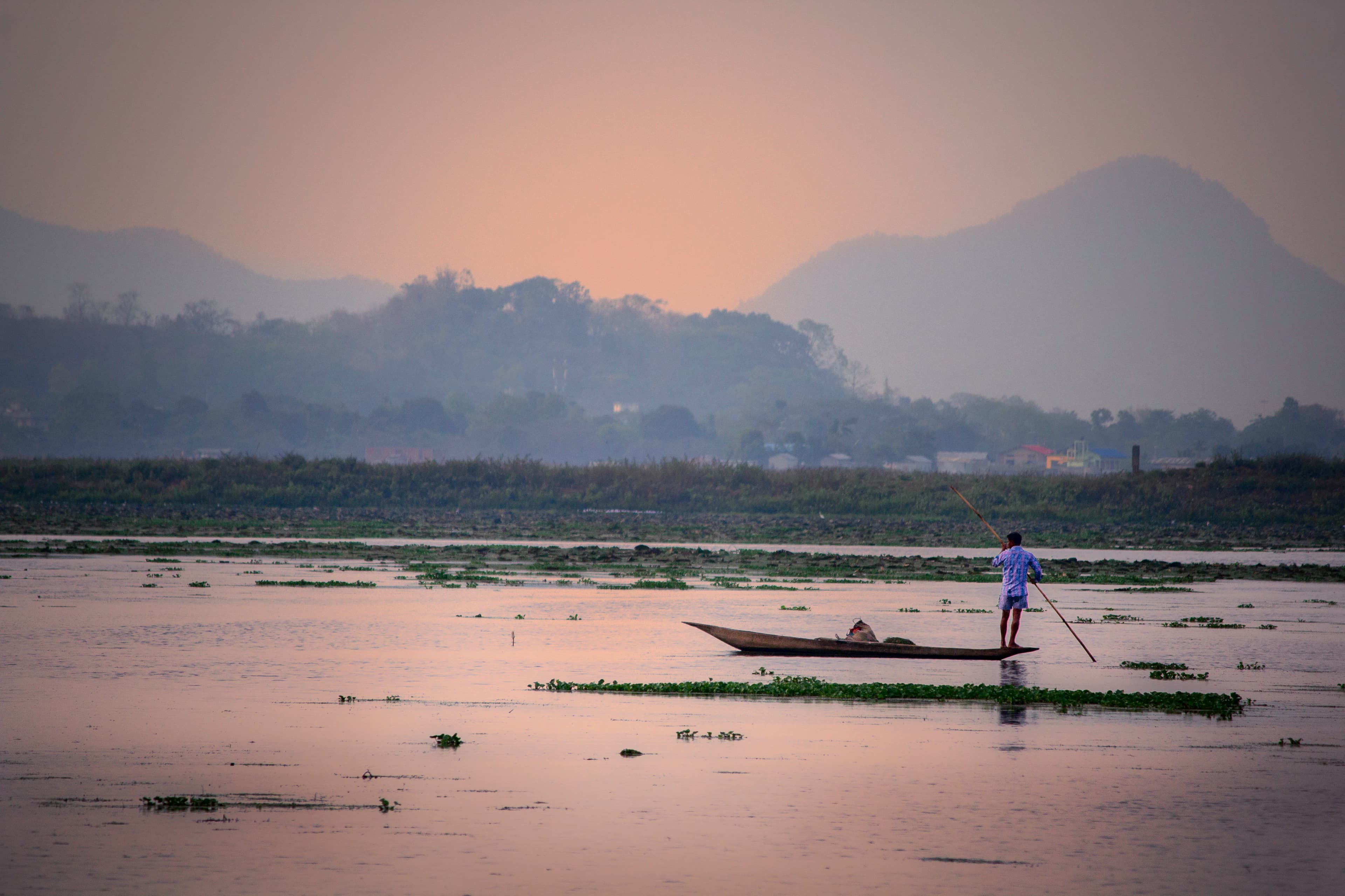 Man rows boat on calm water at sunset