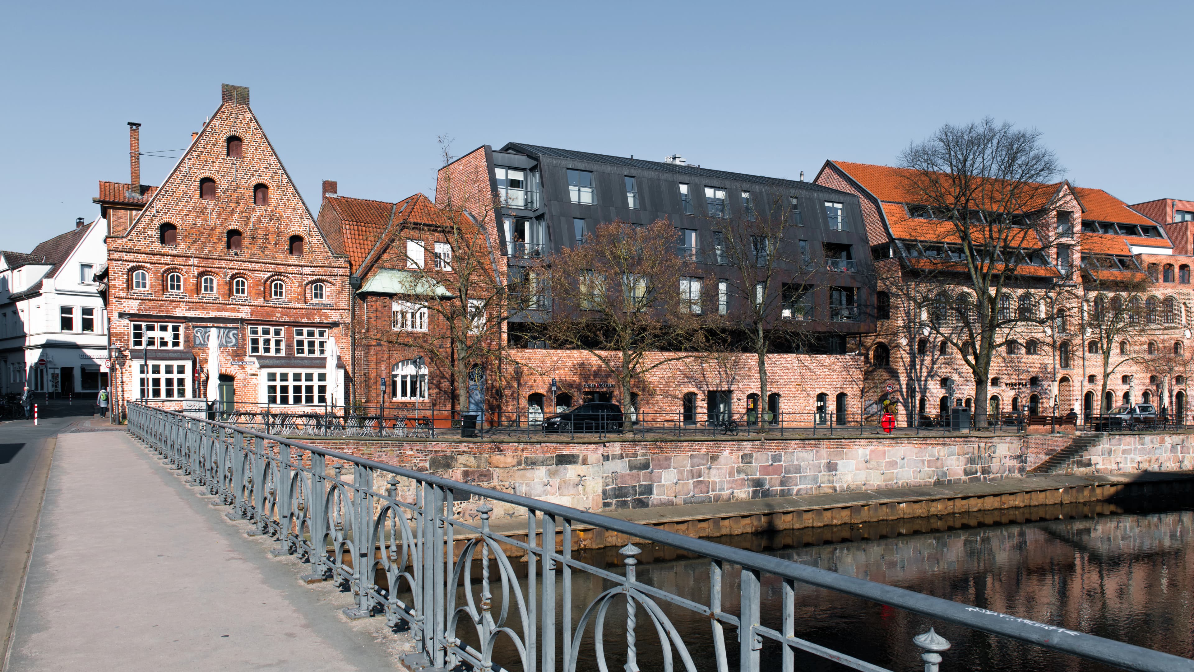 Historic buildings line a river with a bridge in foreground