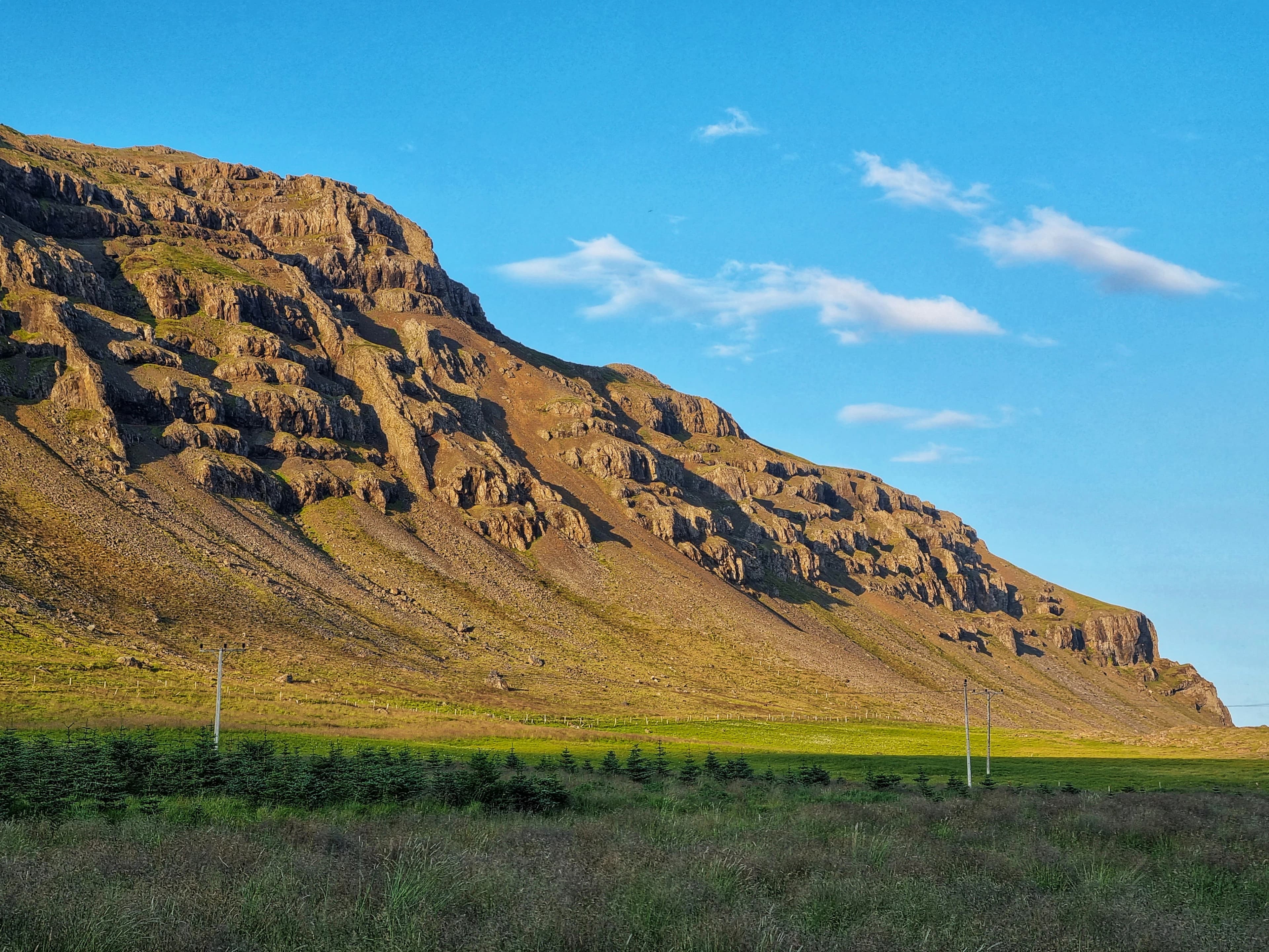 green grass field near brown mountain under blue sky during daytime
