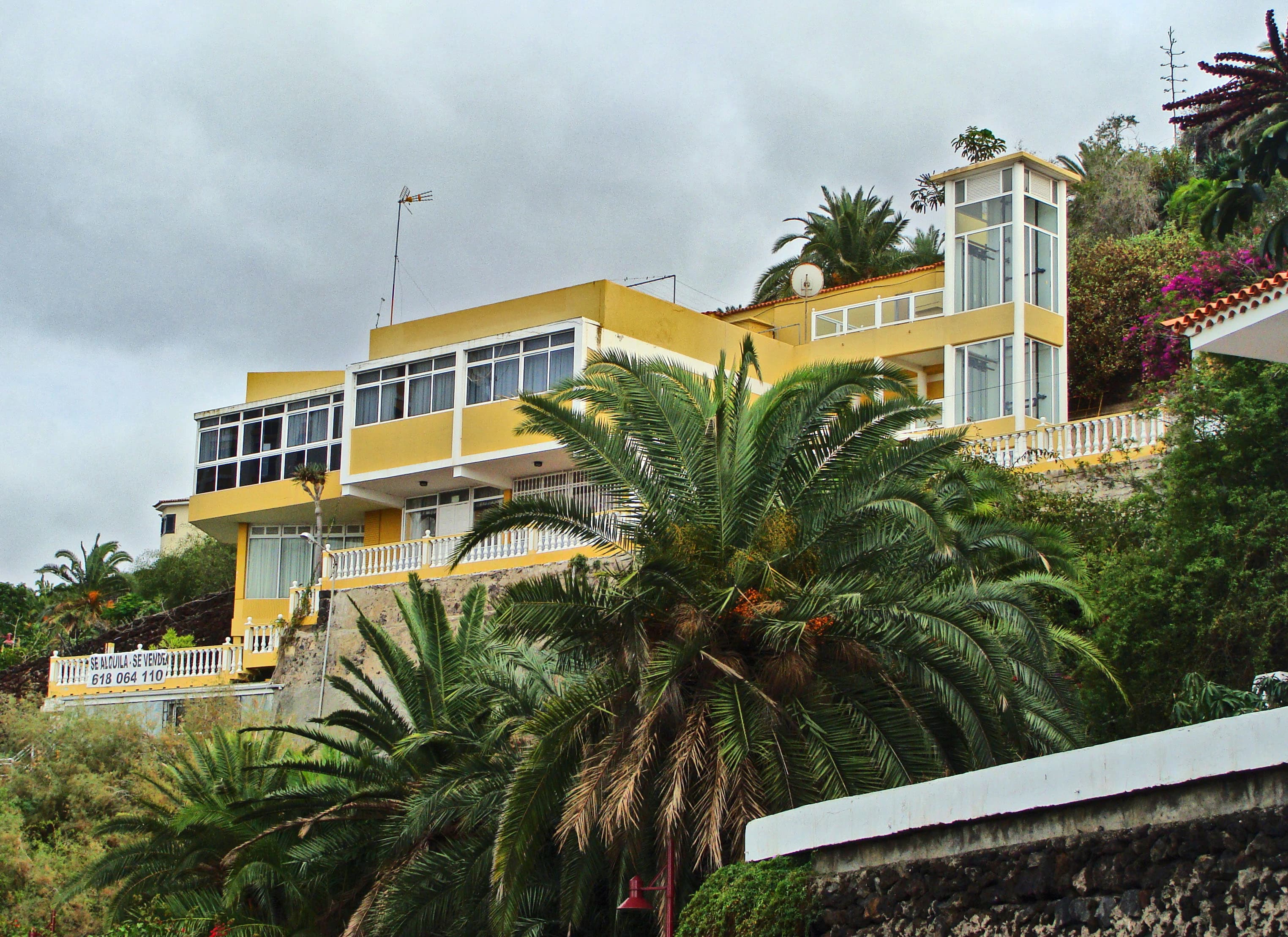 a yellow house on a hill with a palm tree in front of it