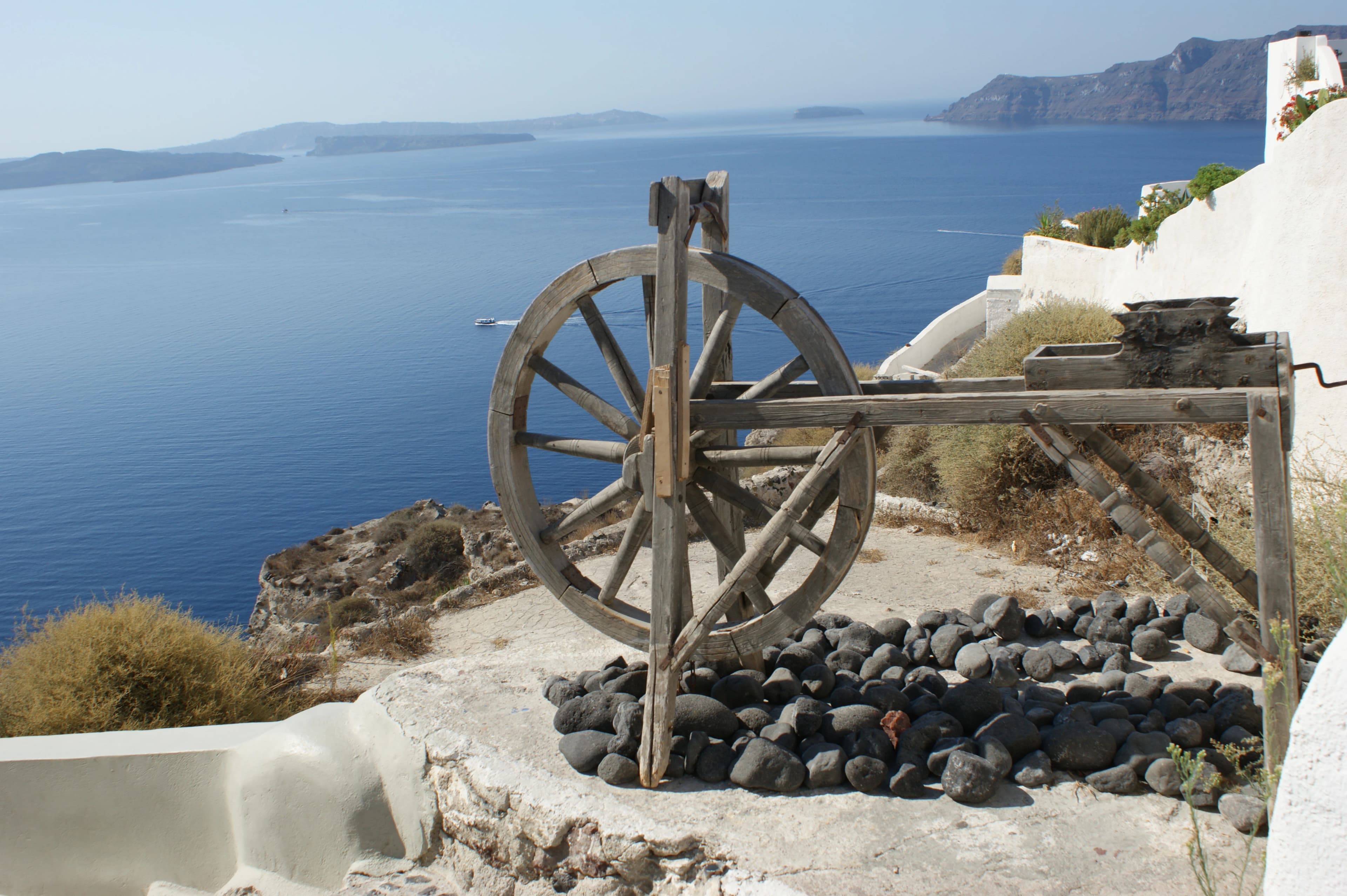 a water wheel sitting on top of a hill next to a body of water