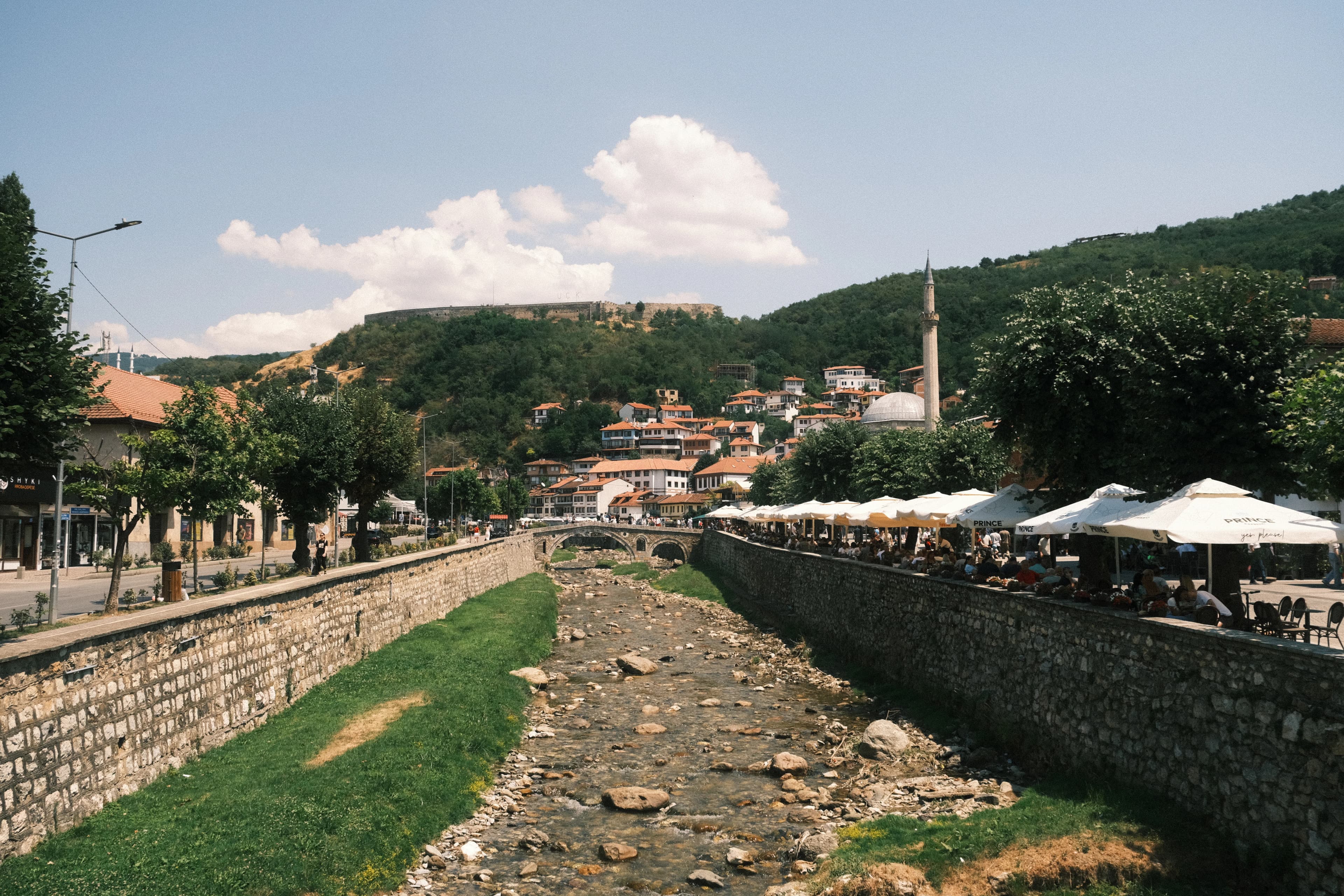A dry riverbed runs through a town with hills behind.