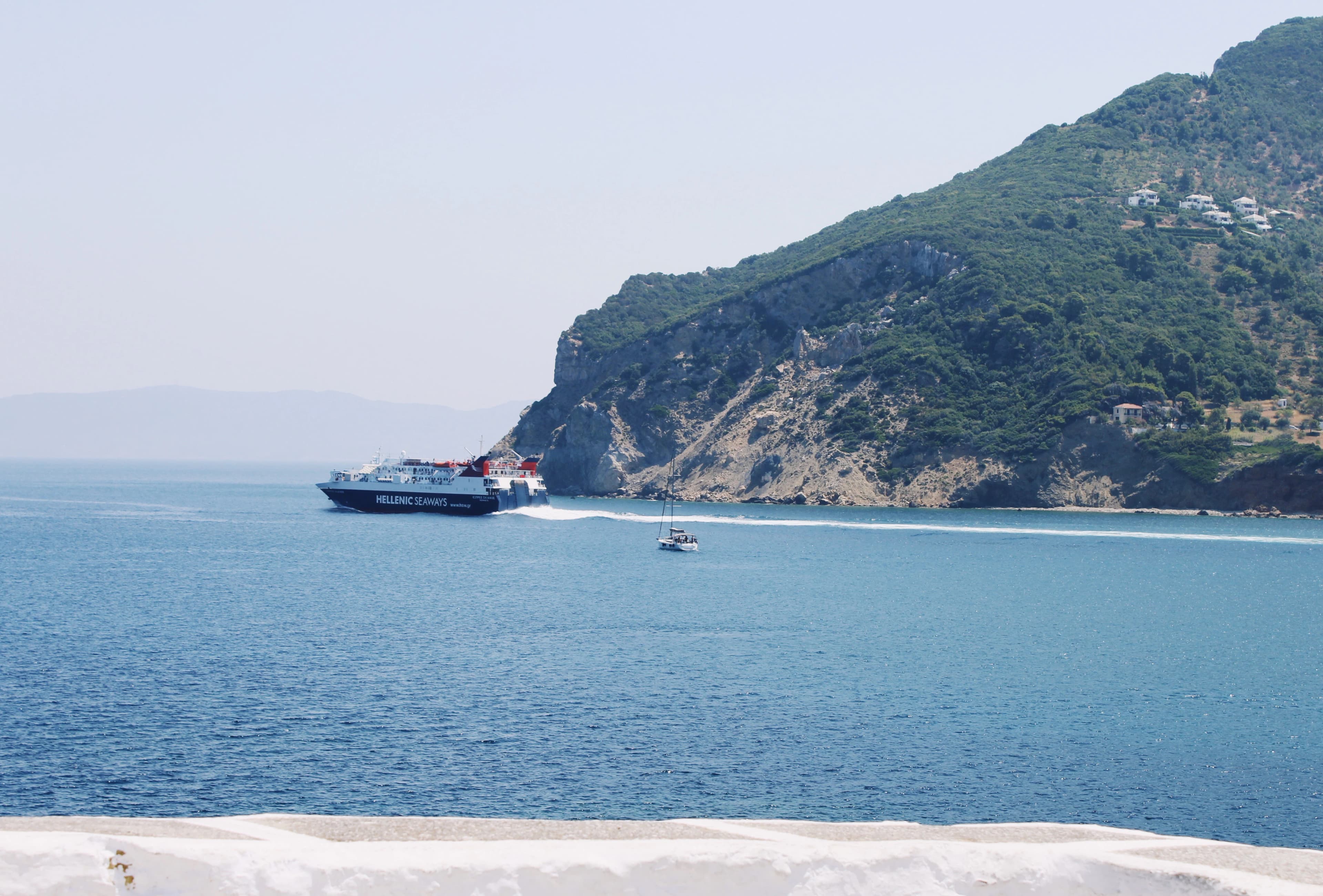 white and black boat on sea near green mountain during daytime