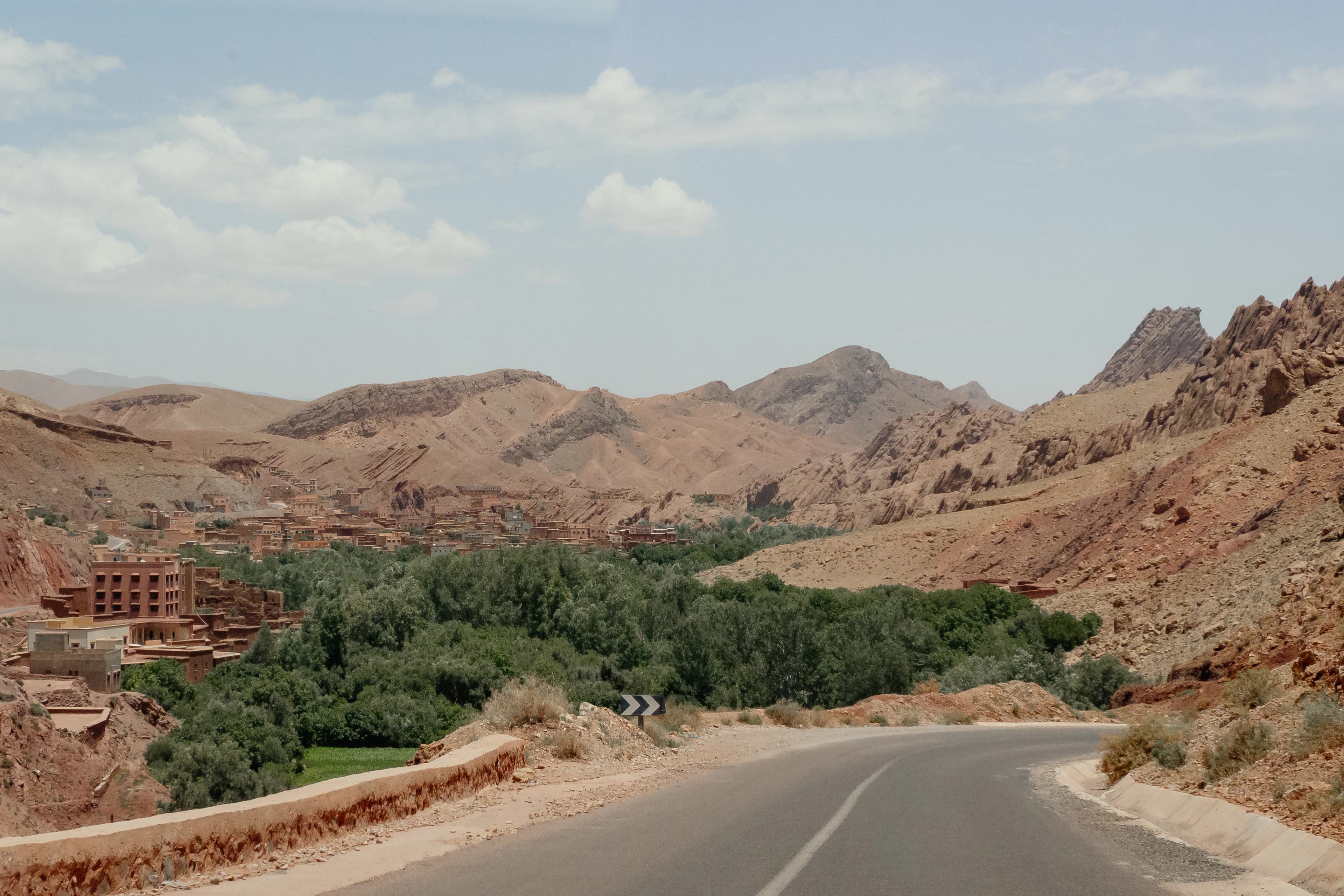 Winding road through arid desert landscape with greenery.
