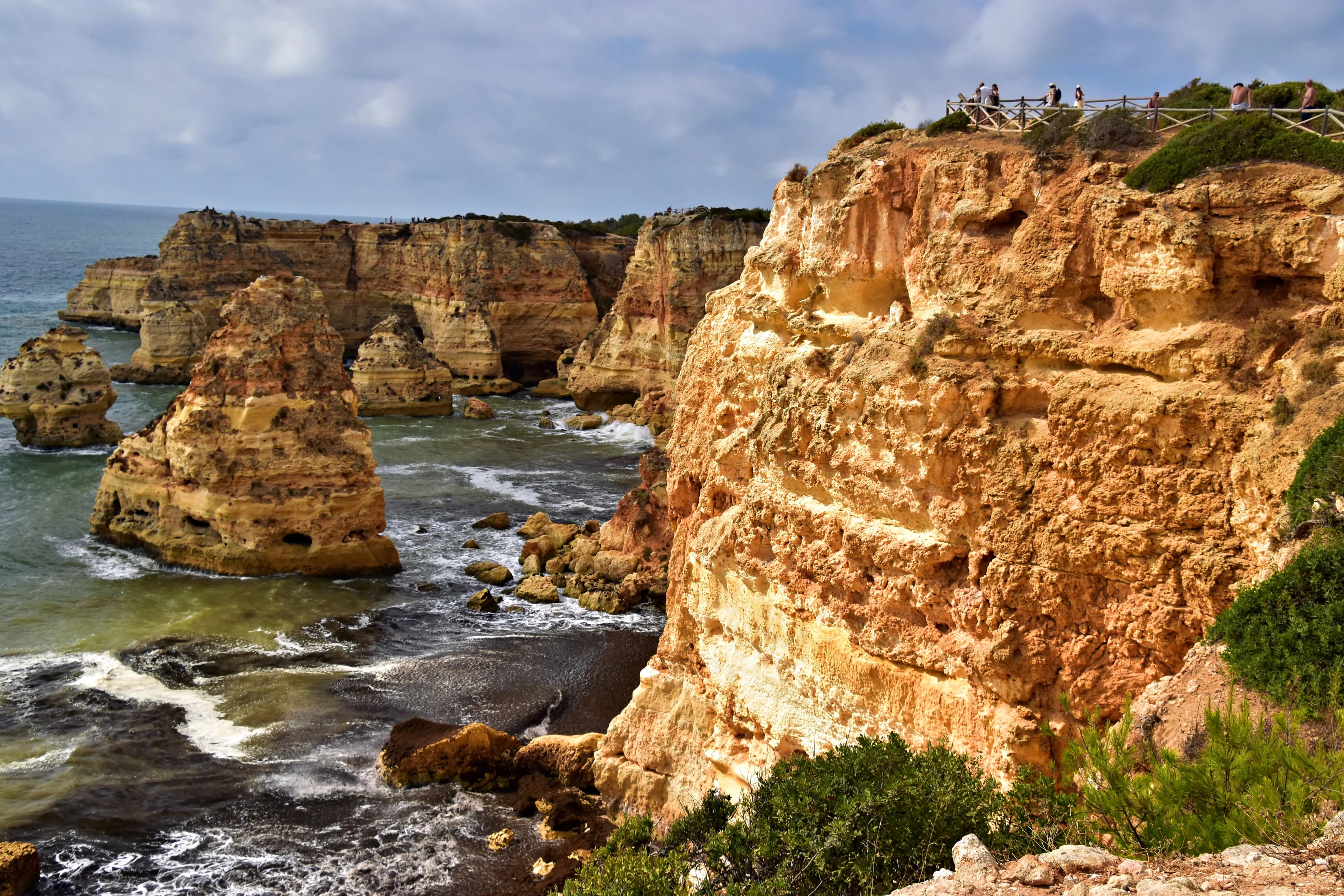 Jagged cliffs meet the ocean waves under a cloudy sky.